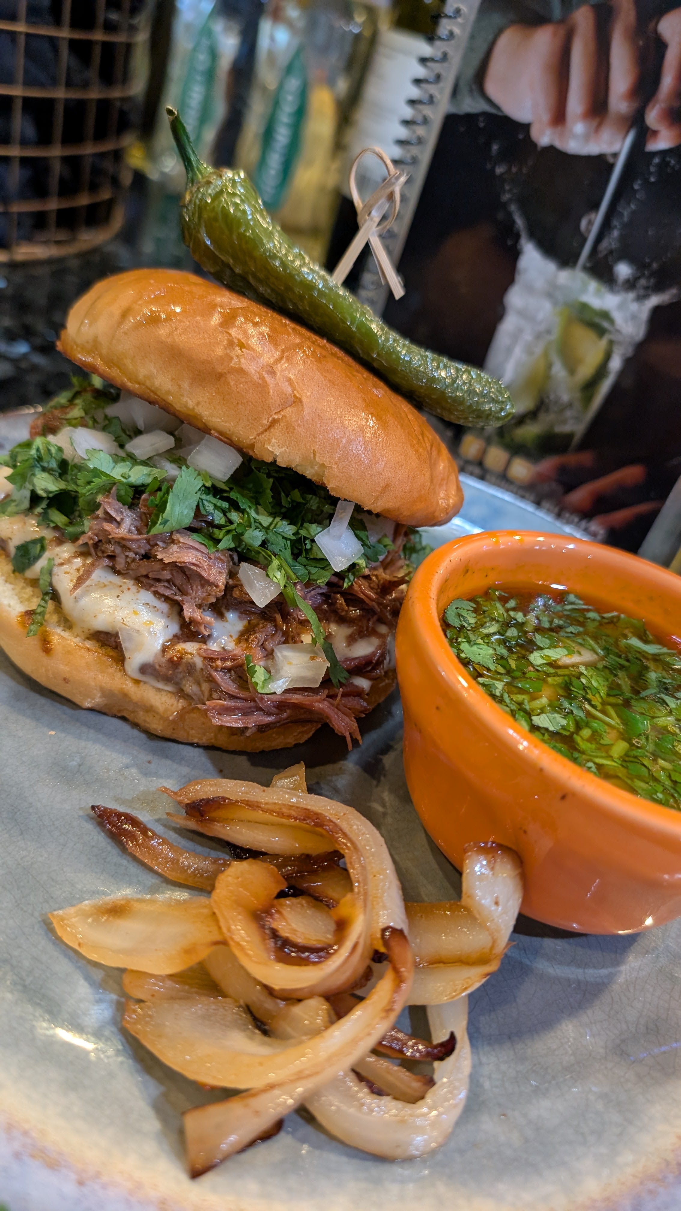 A birria burger served with consomme and grilled onions.