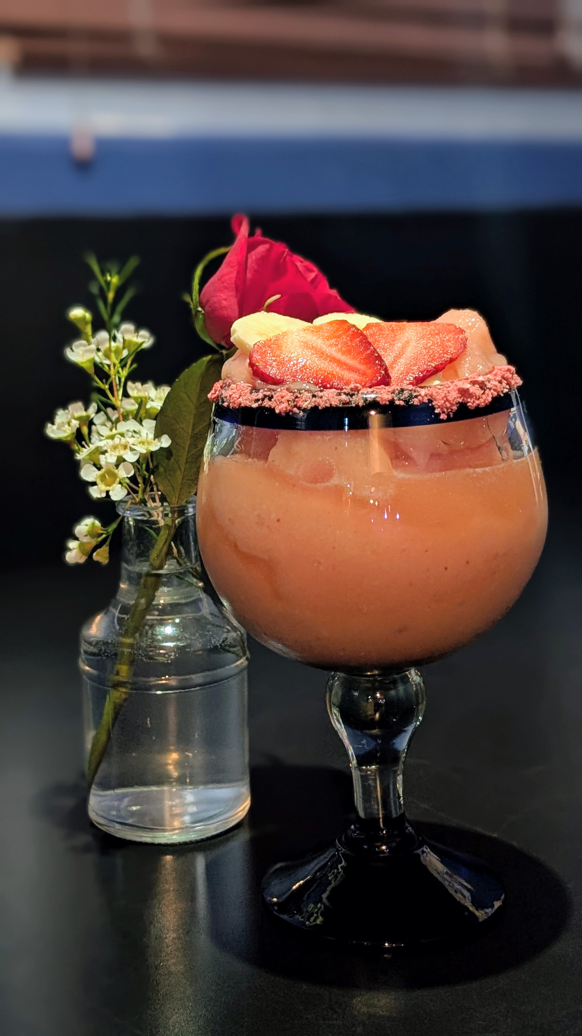 A pink strawberry cocktail garnished with fresh fruit and a rose.